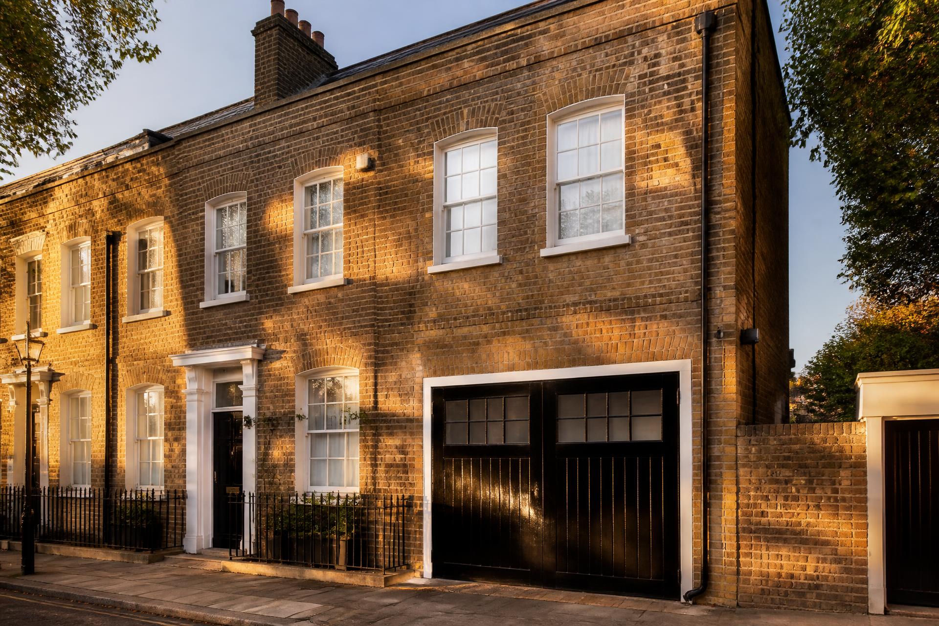 Golden-hour view of a classic Kensington brick terraced house with a glossy black timber garage door and white-painted surround
